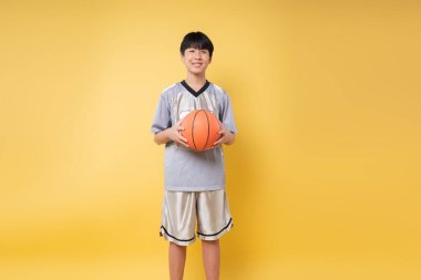 Spor kıyafetlerini giymiş genç bir basketbol meraklısı elinde parlak bir basketbol arkaplanı tutuyor.