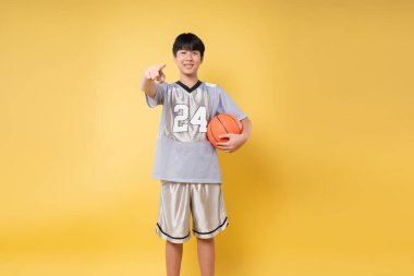 Elinde basketbol topuyla gülümseyen ve sarı arka planı işaret eden bir gencin tam karesi.