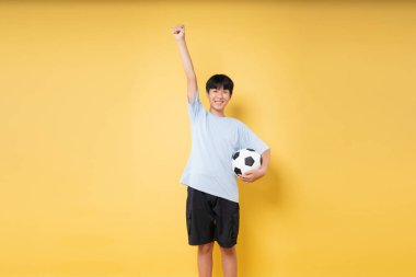 Genç adam kutlama için elini kaldırıyor. Bir futbol topunu canlı sarı bir zemine dayayıp gülümsüyor.