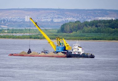 Bir itici bir nicke kum, Volga Nehri üzerinde yüzen bir vinç ile yüklenir. Volgograd.                              