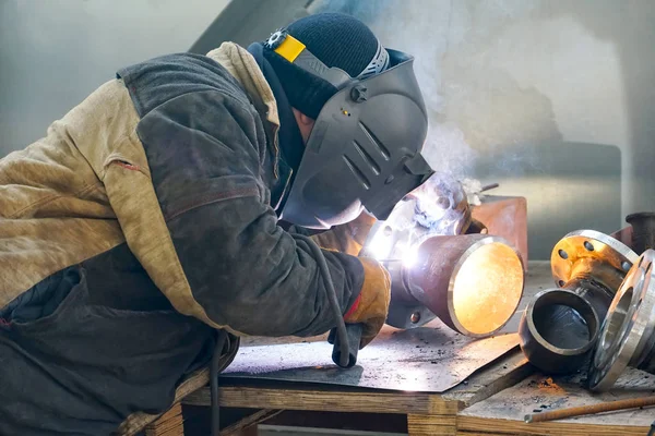 The professional welder works with manual-arc welding. Welds the pipe with the transition DN150. Butt weld.