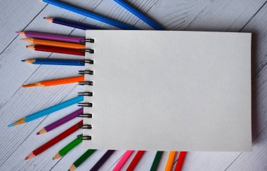 Beyaz ahşap arka plan üzerine açık sac not ve renkli kalemler.