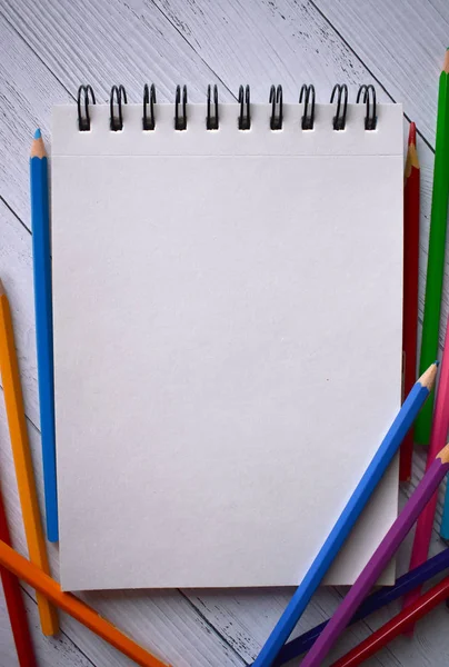 Clear sheet note and colour pencils on white wood background.