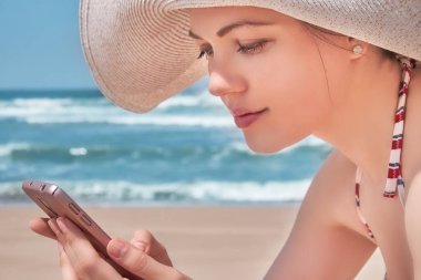 Kumsalda onu cep telefonuyla şapkalı güzel kadın