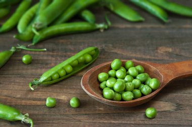 Bir tahta kaşık bezelye bir masada taze yeşil bezelye.