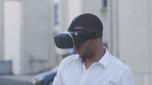 Joven afroamericano con camisa blanca que tiene experiencia del casco de la realidad virtual. Empresario en gafas VR en la ciudad. Al aire libre. Retrato — Vídeo de stock