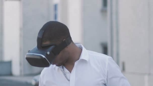 Joven afroamericano con camisa blanca que tiene experiencia del casco de la realidad virtual. Empresario en gafas VR en la ciudad. Al aire libre. Retrato — Vídeos de Stock