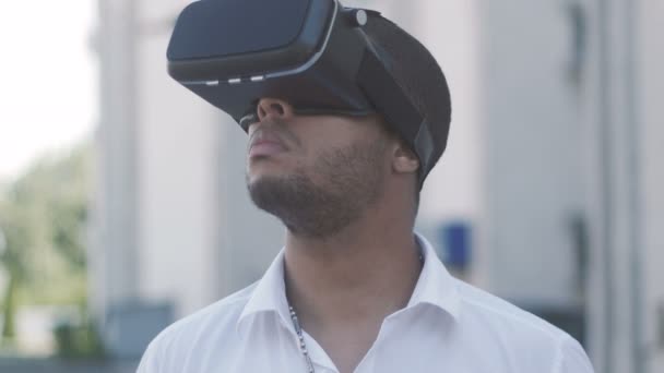 Gros plan du jeune homme d'affaires afro-américain en chemise blanche utilisant le casque de réalité virtuelle dans la ville. Extérieur . — Video