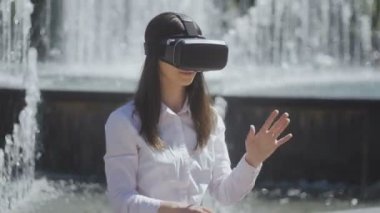 Sanal oyunlar oynayan ve bir çeşme bir şehir sokakta bir arka plan video izleme vr gözlük, kulaklık, genç kadın kapatmak