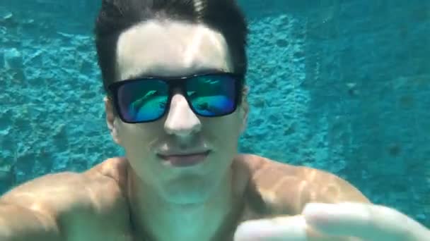 バカンスの若い男はサングラスでプールにダイブします。彼は泳ぐし、ビデオで自分自身を脱ぐ. — ストック動画