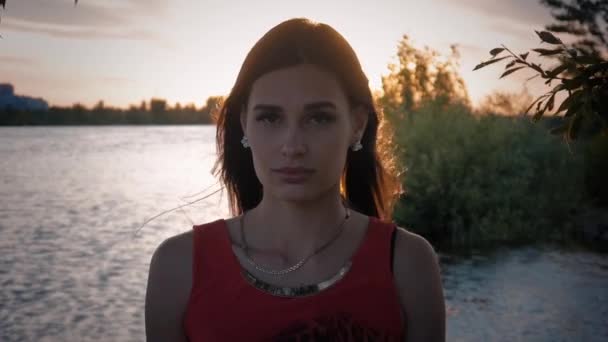 Портрет привлекательной молодой женщины вечером на закате на фоне пруда — стоковое видео