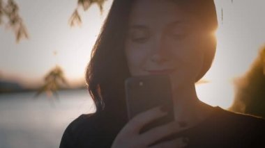 bir göl günbatımı bir arka plan üzerinde akıllı telefon kullanan genç oldukça esmer kadın