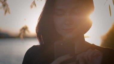bir göl günbatımı bir arka plan üzerinde akıllı telefon kullanan genç oldukça esmer kadın