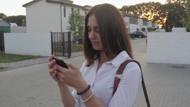 Jeune femme utilisant un smartphone sur fond de maisons de ville dans un quartier résidentiel — Video