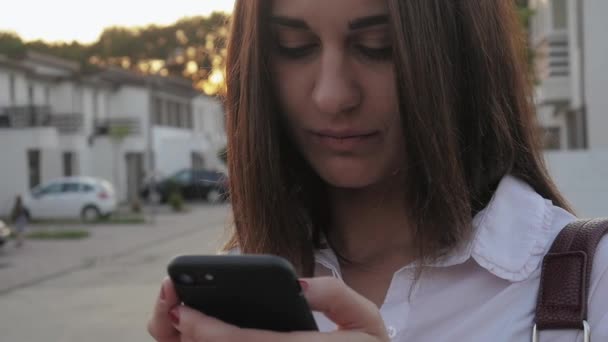 Jonge vrouw met behulp van smartphone op achtergrond van herenhuizen in woonwijk — Stockvideo