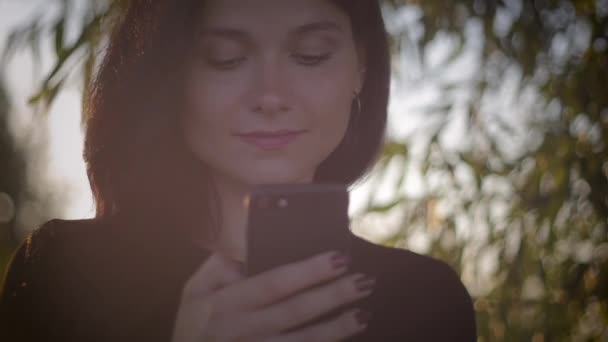 Jeune jolie femme brune utilisant un smartphone sur un fond de coucher de soleil sur un lac — Video