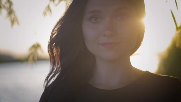 Retrato de una joven guapa morena sobre un fondo al atardecer en un lago — Vídeos de Stock