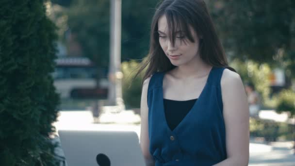 Junges Mädchen arbeitet mit Laptop in einem Park auf einer Bank auf einer Straße in der Stadt Hintergrund — Stockvideo