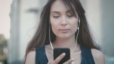 smartphone kullanarak ve kulaklıklar sokak arka plan açık müzik dinlemek genç güzel kadın portresi