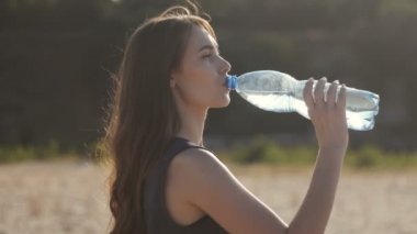 Genç kadın bir sıcak yaz gününde susuz suyu plastik şişeden içer.