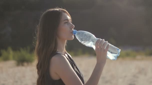 女孩旅行者在炎热的沙地上从自然界的塑料瓶中喝水 日落时 女孩感觉口渴与水的断裂 — 图库视频影像