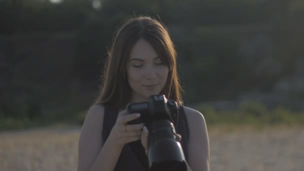 女摄影记者使用专业相机拍摄自然照片。女孩正在做一个镜头, 看着相机上的照片 — 图库视频影像