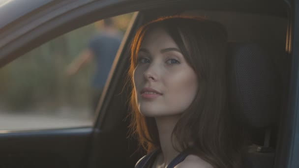 Gün batımı arka plan üzerinde sürüş sırasında arabada oturan genç kadın portresi — Stok video
