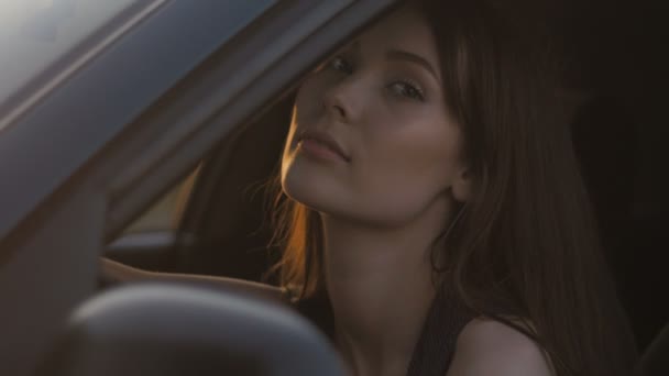 Portret van de jonge vrouw zitten in de auto tijdens het rijden op de zonsondergang achtergrond — Stockvideo