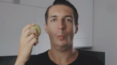 Genç adam yeme yeşil elma evde mutfakta. Taze bir elma yeme ve kameraya bakarak adam portresi.