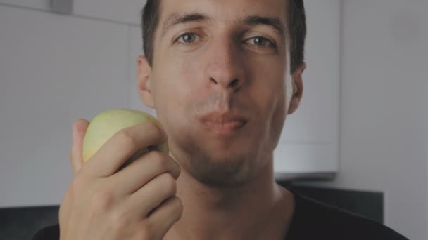 젊은 사람을 먹는 녹색 사과 집에서 부엌에서. 신선한 사과 먹고 카메라를 보고 남자의 초상화. — 비디오