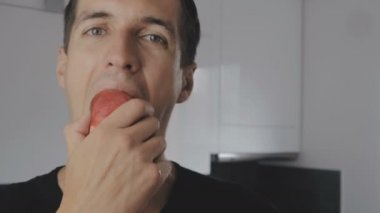 Genç adam yeme kırmızı elma ve bir ani diş ağrısı evde mutfakta hissediyor.