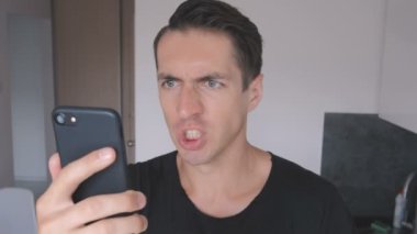 Kızgın genç adam siyah T-shirt agresif smartphone evde mutfakta kullanır..