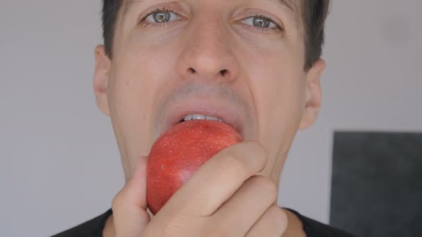 Primo piano del giovane che mangia mela rossa a casa in cucina. Ritratto di ragazzo che mangia una mela fresca e guarda la macchina fotografica . — Video Stock
