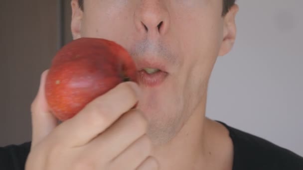 Primer plano de un joven comiendo manzana roja en casa en la cocina. Retrato de un chico comiendo una manzana fresca y mirando a la cámara . — Vídeos de Stock