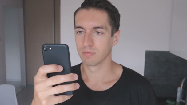 검은 티셔츠에 젊은 남자는 부엌에서 집에서 스마트폰 사용. — 비디오