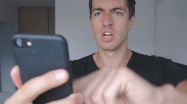 Kızgın genç adam siyah T-shirt agresif smartphone evde mutfakta kullanır..