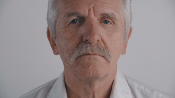 Primer plano Retrato del hombre mayor con bigote mira a la cámara en el fondo blanco — Vídeos de Stock