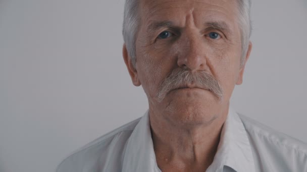 Primer plano Retrato del hombre mayor con bigote mira a la cámara en el fondo blanco — Vídeos de Stock
