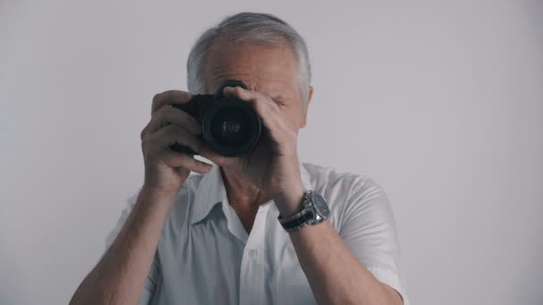 Gris chevelu senior homme photographe prend des photos avec son appareil photo à fond blanc — Video