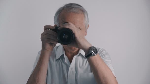 Grå korthårig Senior mannen fotograf tar bilder med sin fotokamera på vit bakgrund — Stockvideo
