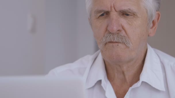 Крупный план портрета седовласого пожилого человека с усами, работающего за ноутбуком в офисе и пьющего кофе — стоковое видео