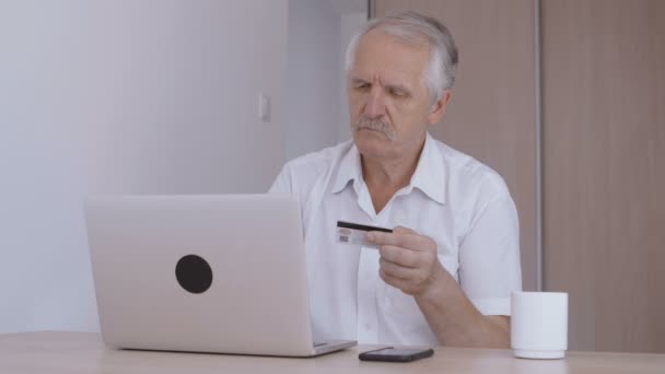 Hombre mayor de compras en línea en casa en el ordenador portátil, escribiendo el número de tarjeta de crédito — Vídeo de stock