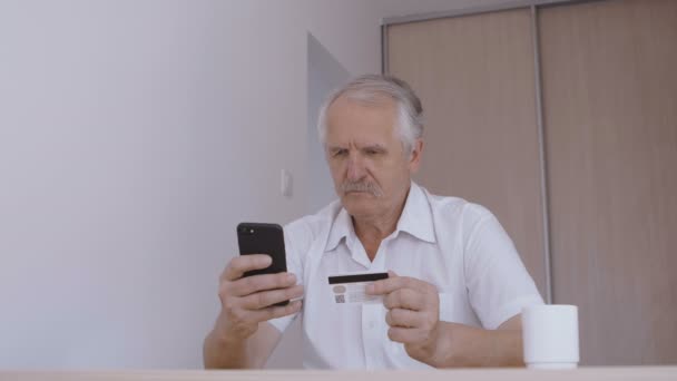 Hombre mayor de compras en línea con tarjeta de crédito utilizando el teléfono inteligente en casa. Aplicación móvil de banca en línea — Vídeos de Stock