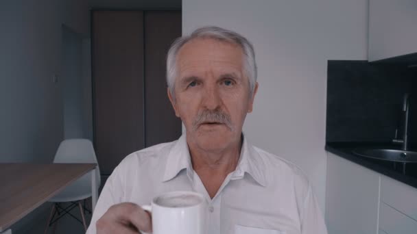 Портрет старшого чоловіка з вусами п'є каву вдома на кухні вранці — стокове відео
