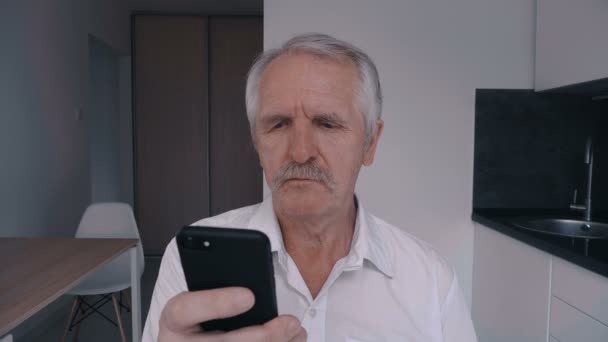 Retrato del hombre mayor con bigote usando teléfono inteligente en casa en la cocina — Vídeos de Stock