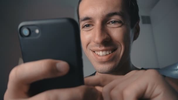 Šťastný mladý muž s úsměvem používá smartphone doma v kuchyni. — Stock video