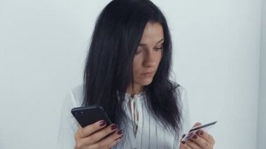 Genç bir kadın internet üzerinden kredi kartı ve akıllı telefonuyla alışveriş yapıyor.