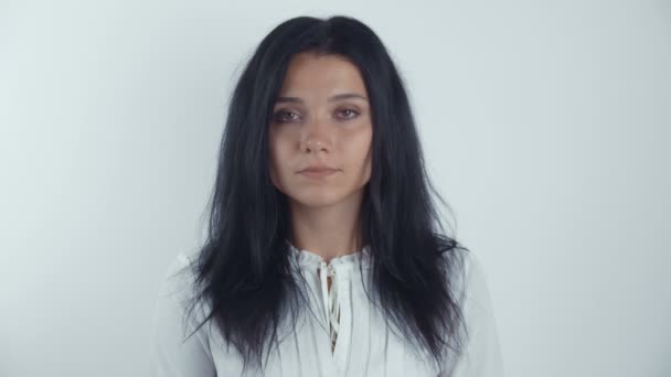 Портрет юной брюнетки, смотрящей в камеру на белом фоне — стоковое видео