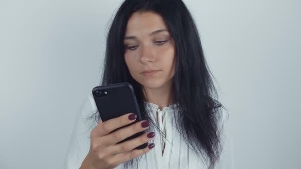 Portrét mladé ženy brunetka pomocí smartphone na bílém pozadí — Stock video