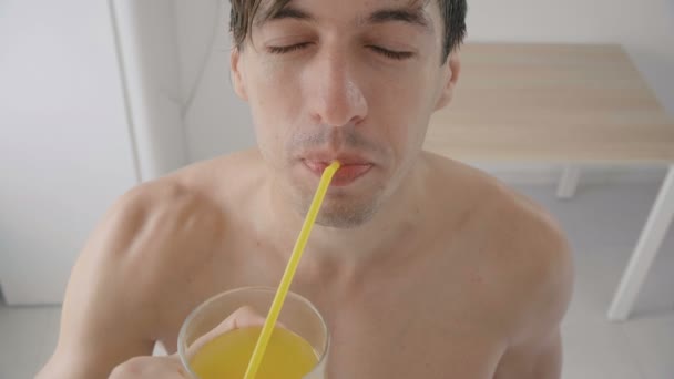 Ung man dricker uppfriskande orange soda genom en slang på het sommar i köket — Stockvideo